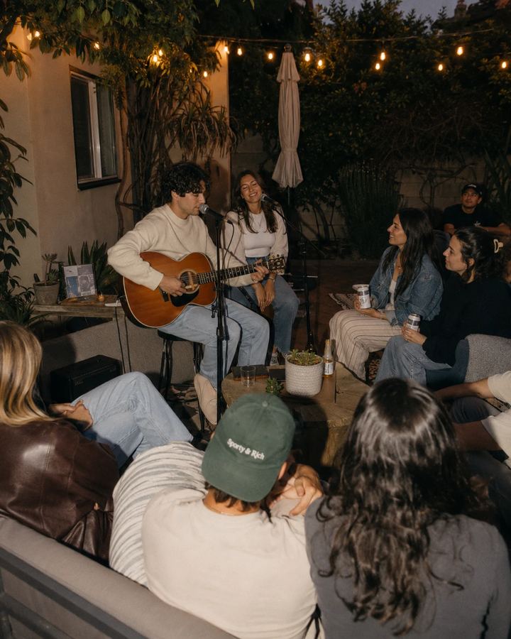 An acoustic set under string lights at a backyard show